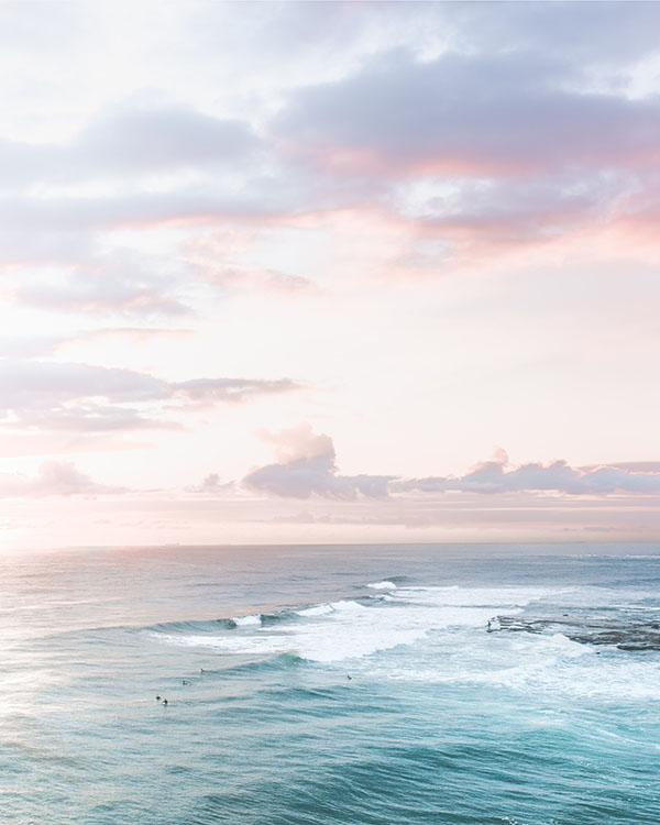 Surfers in the sea from a distance with an early morning sky